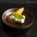 Dessert with white quenelles, praline crumble and a caramel crisp on a dark plate at Restaurante Puerto Blanco, Calpe